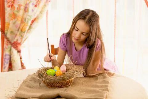 Cute girl decorating easter eggs in basket Foto stock