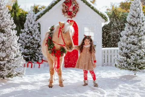 Cute girl with deer horns standing with a pony horse under the snow. Stock Photos