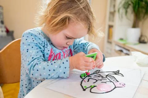 Cute girl drawing a fish using glass colors at home. Stock Photos