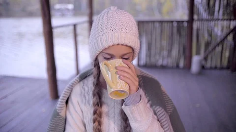 Cute girl drinking hot tea at the lake wrapping herself in plaid Stock Footage 70551406