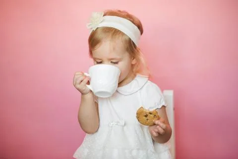 Cute girl has breakfast, eats cookies and drinks kefir from a cup Stock Photos