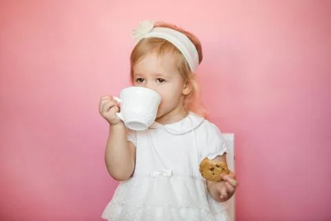 Cute girl has breakfast, eats cookies and drinks kefir from a cup Stock Photos