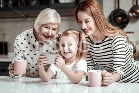 Cute girl holding modern smartphone and taking selfies with family Stock Photos