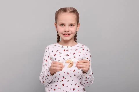 Cute girl holding tasty fortune cookie with prediction on light grey backgrou Stock Photos