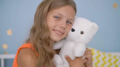 Cute girl hugging teddy bear while sitting on bed at home Stock Footage 93668043