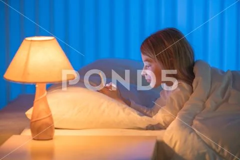 The cute girl lay on the bed and phone. Evening night time Stock Photos