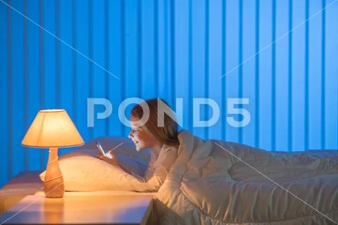 The cute girl lay on the bed and phone. Evening night time Stock Photos