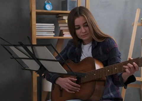 Cute girl is learning to play classical guitar while sitting at a music stand Stock Photos