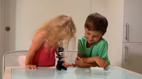 A cute girl is looking through a microscope and then letting a boy to have look Stock Footage 129118527