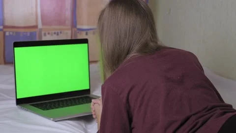 A cute girl is lying on the bed, in front of her is a laptop with a green screen Video stock 201533926