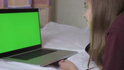 A cute girl is lying on the bed, in front of her is a laptop with a green screen Stock Footage 207240662