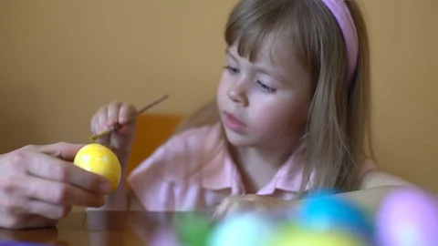 Cute girl paints an Easter egg. Mom helps her daughter to draw on the egg. Stock Footage 104991084