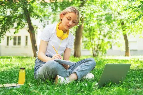 Cute girl is sitting in the park in headphones with a laptop Stock Photos
