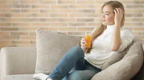 Cute girl sitting on sofa drinking juice looking at camera and smiling Stock Footage 34115731