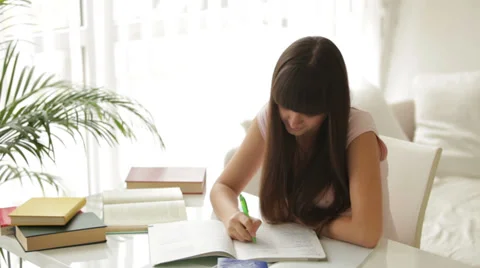 Cute girl sitting at table studying and writing in notebook Video stock 29638053