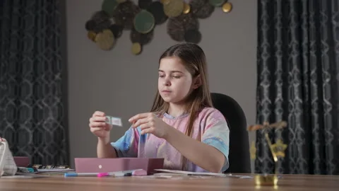 Cute girl sitting at table, thinking which sticker to choose to stick on Stock Footage 266805101