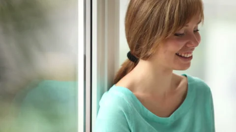 Cute girl sitting by window drinking juice using cellphone looking at camera  Stock Footage 33851230