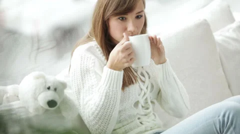 Cute girl sitting by window drinking tea looking at camera and smiling. Panning Stock Footage 34150064