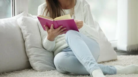 Cute girl sitting by window reading book looking at camera and smiling. Panning Stock Footage 34149953