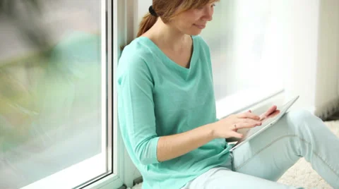 Cute girl sitting by window using touchpad looking at camera and smiling Stock Footage 33851064