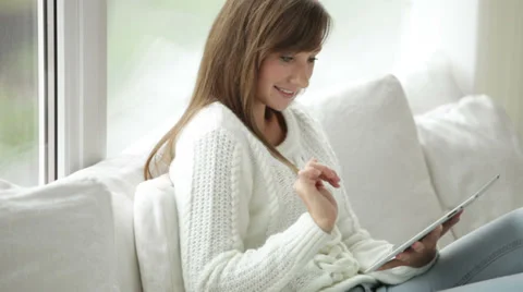 Cute girl sitting by window using touchpad looking at camera and smiling Vídeos de archivo 34149946