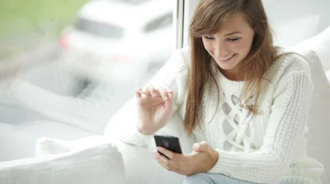 Cute girl sitting by window using mobile phone looking at camera and smiling Stock Footage 34149954