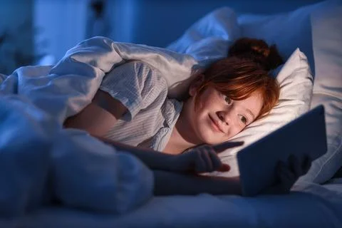 Cute girl with tablet computer lying in bed at night Stock Photos