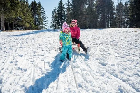 Cute girl trying to pull her mother on snow sledge. Stock Photos