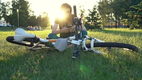 Cute girl using app on smartphone sitting near a bicycle at sunset in the city Stock Footage 78480538