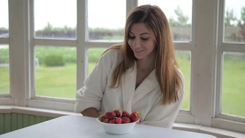 Cute girl in a white coat, sitting on the veranda and eating strawberries. Stock Footage