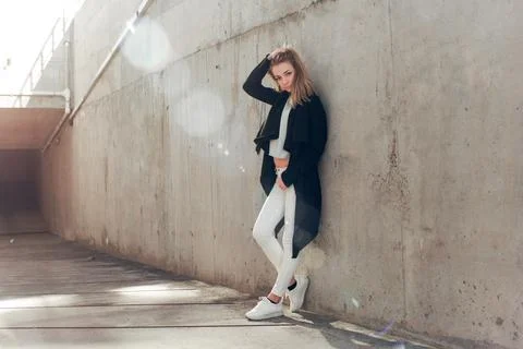 Cute girl in white pants posing leaning against a concrete wall Stock Photos