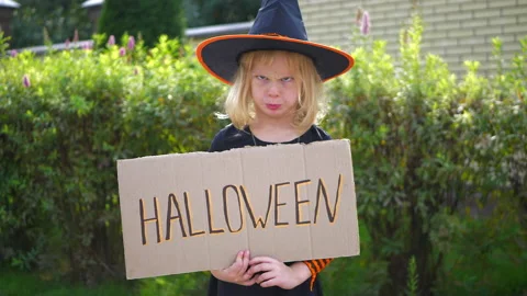 Cute girl in witch hat making faces and holding cardboard with halloween text. Stock Footage 183538325