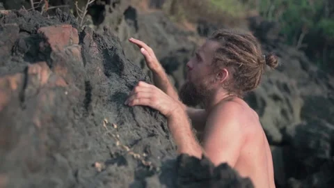 A cute guy with an open torso and an attractive appearance climbs on the stones. Video stock 234021803