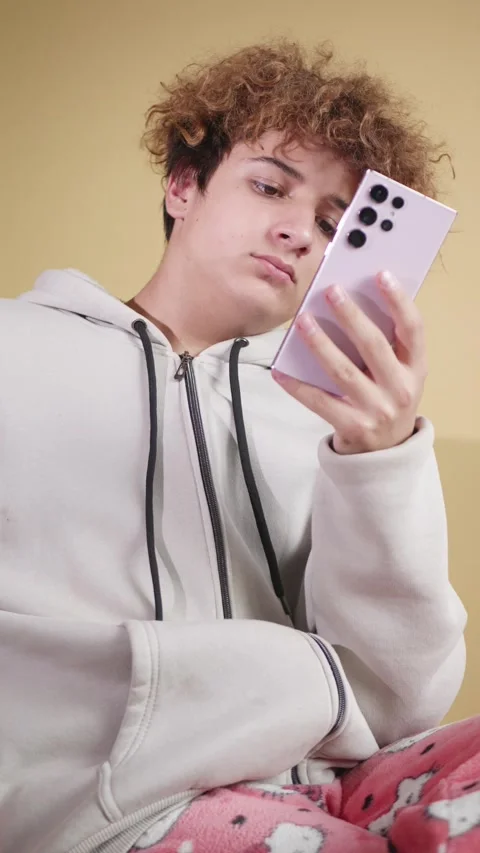 A cute guy with a smartphone is sitting on a honey background. Vertical video. Stock Footage 321422876