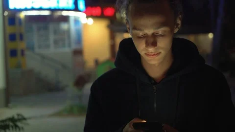 Cute handsome young boy using smartphone outdoors at night, 4k Stock Footage 98502757