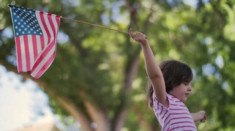 Cute happy 5 year old American girl waving USA flag on suburban city park street Stock Footage
