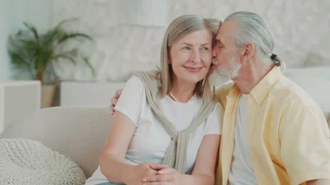Cute happy elderly couple smiling and hugging relaxing at home sitting on the Vídeos de archivo 224530437