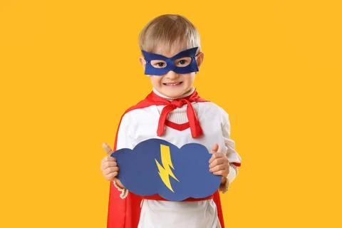 Cute happy little boy dressed as superhero with cloud and lightning on yellow Foto stock