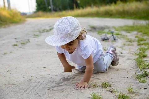 Cute happy toddler in a cap crawls on all fours along a country road in the s Stock Photos