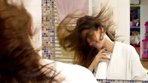 Cute happy young woman in bathroom blow drying long hair singing Stock Footage