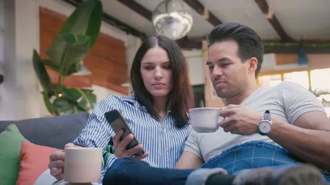 Cute Hispanic couple lying in cosy living room, using new application on mobile Stock Footage 105759270