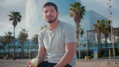Cute Hispanic man sitting at urban area and enjoying fresh melon fruit with Stock Footage 108443564
