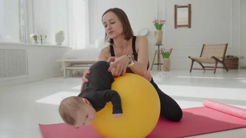 Cute infant boy doing exercises lying on fitness ball while mother holding her 動画素材 151346106