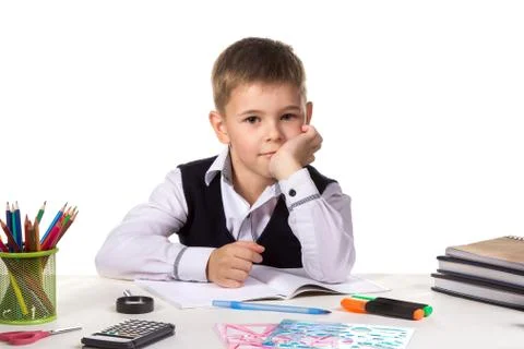 Cute intelligent pupil sitting at the desk with hand under the chin surrounded Stock Photos