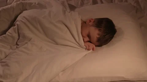 Cute kid boy is sleeping happily on a pillow under a blanket in the evening Vidéo 263978883