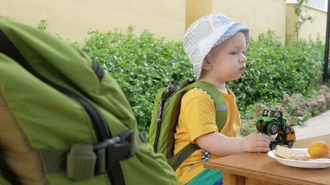 A cute kid eats outdoors in a cafe. He plays with cars and eats cookies with Stock Footage 76400885