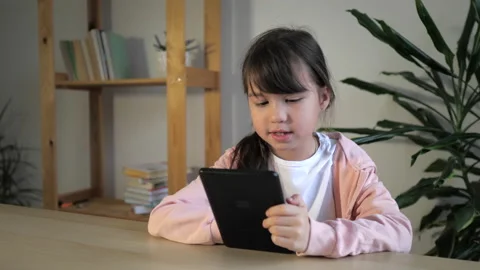 Cute kid girl using digital tablet device sitting by the table at home. Small Stock Footage 165625133