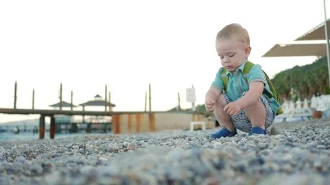A cute kid plays alone by the sea. He carefully touches and examines the colored Stock Footage 76472084