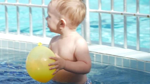 A cute kid plays in a children's pool with an inflatable yellow ball. He walks Stock Footage 76476546