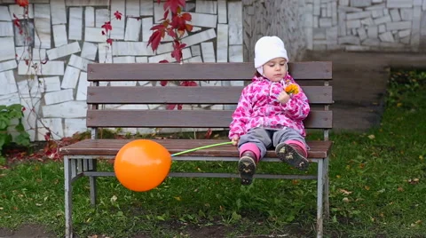Cute kid sitting alone on a bench, holding the flower. Stock Footage 68399425